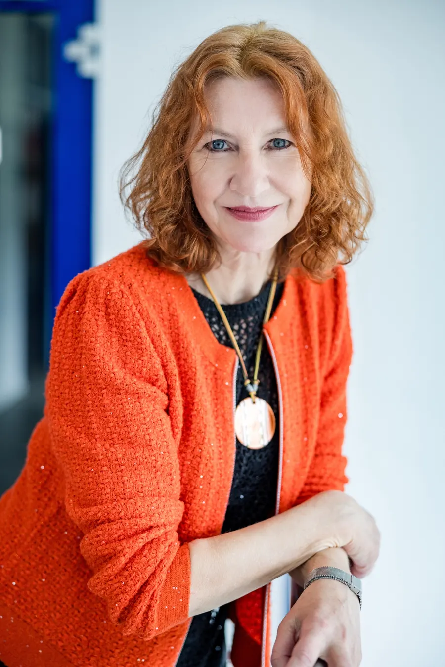 Silvia Ziolkowski im orangen Blazer, lächelnd an ein Geländer gelehnt